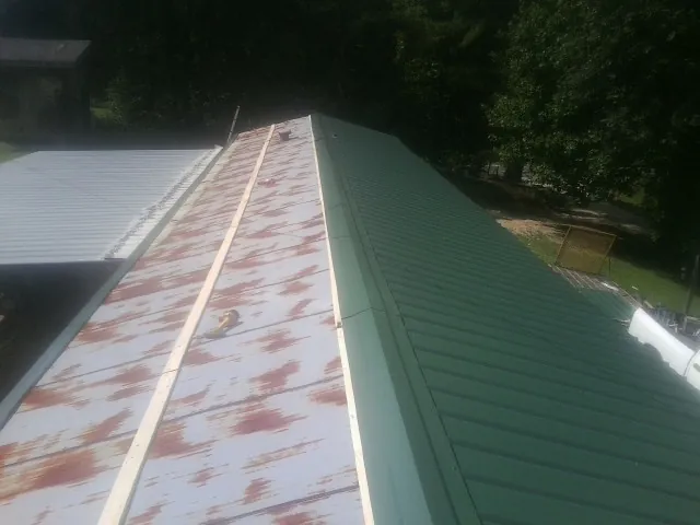 Old rusted panels beside newly installed green metal roofing — Wind Damage Roof Repair by Roofing Brothers in Gretna